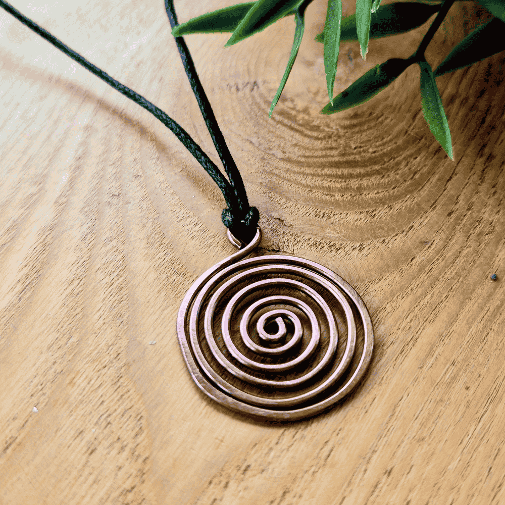 Bronze spiral pendant on a black cord with green leaves in the background