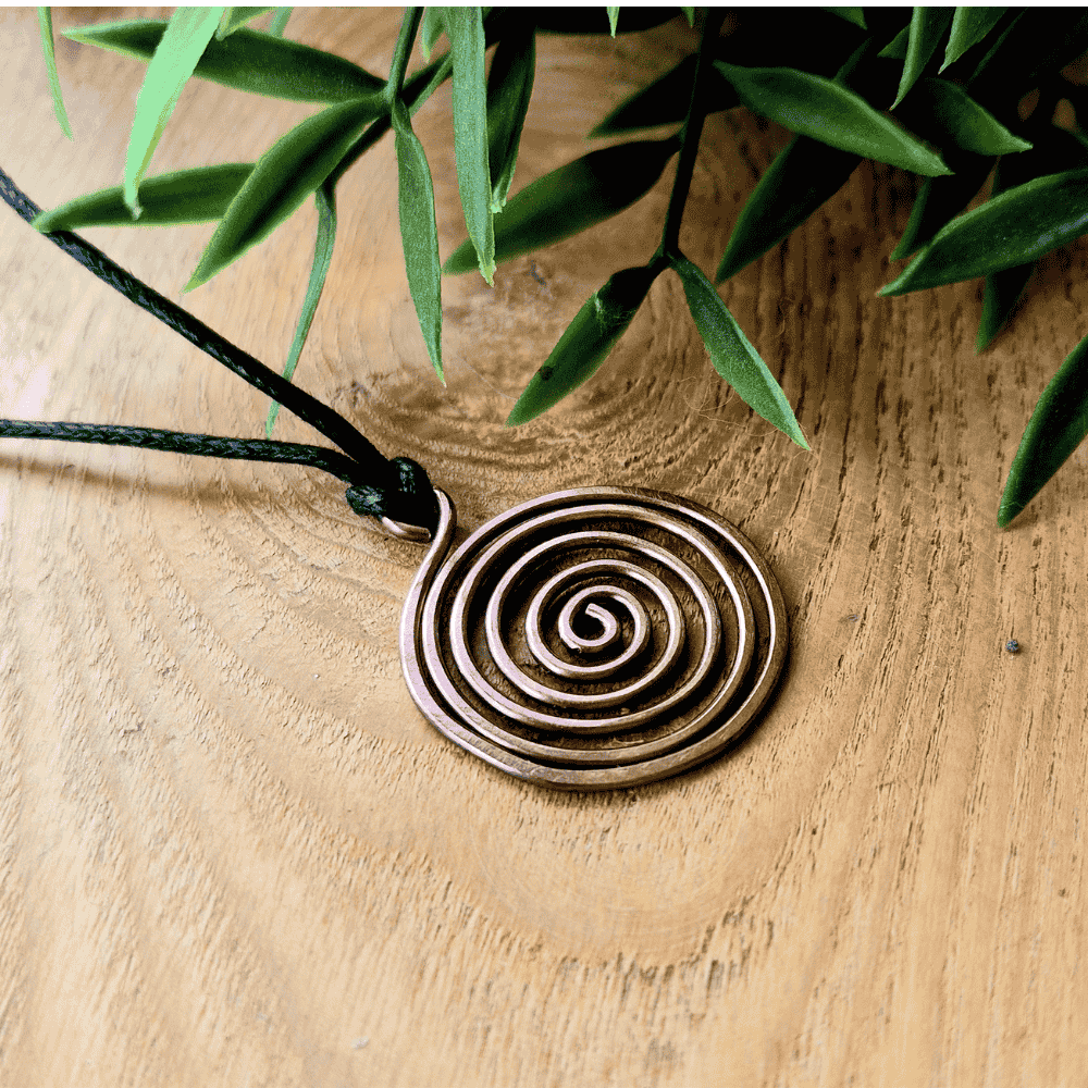 Bronze spiral pendant on a wooden surface with green leaves in the background