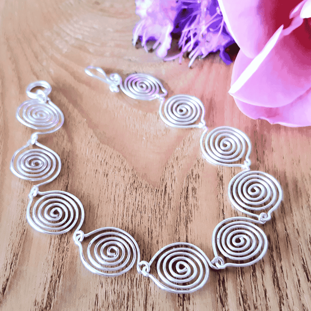 Silver spiral necklace on a wooden surface with pink flowers
