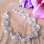 Silver spiral necklace on a wooden surface with pink flowers