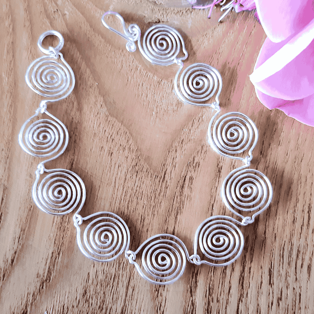 Silver spiral necklace on a wooden surface with pink fabric and flowers.