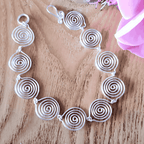 Silver spiral necklace on a wooden surface with pink fabric and flowers.