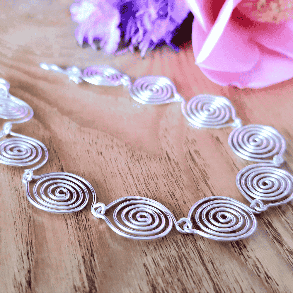 Silver spiral necklace on a wooden surface with flowers in the background
