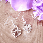 Silver spiral earrings on a wooden surface with purple flowers.
