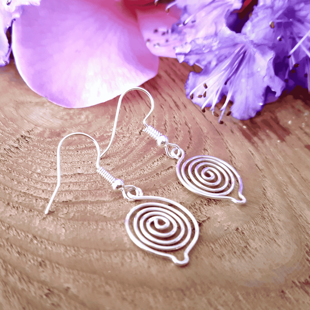 Silver spiral earrings on a wooden surface with purple flowers.