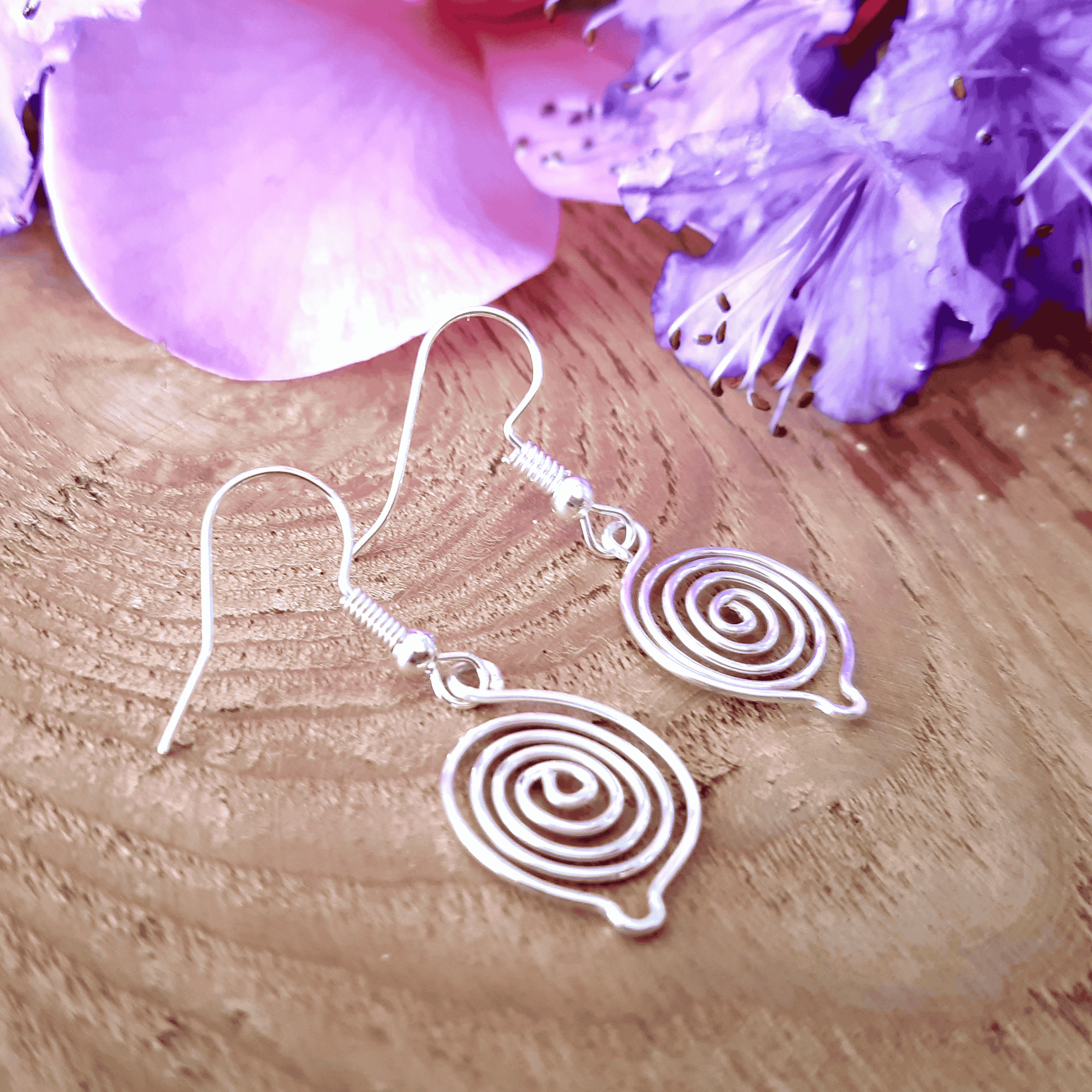 Silver spiral earrings on a wooden surface with purple flowers.