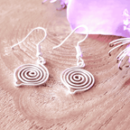 Silver spiral earrings on a pink wooden surface with a purple fabric background