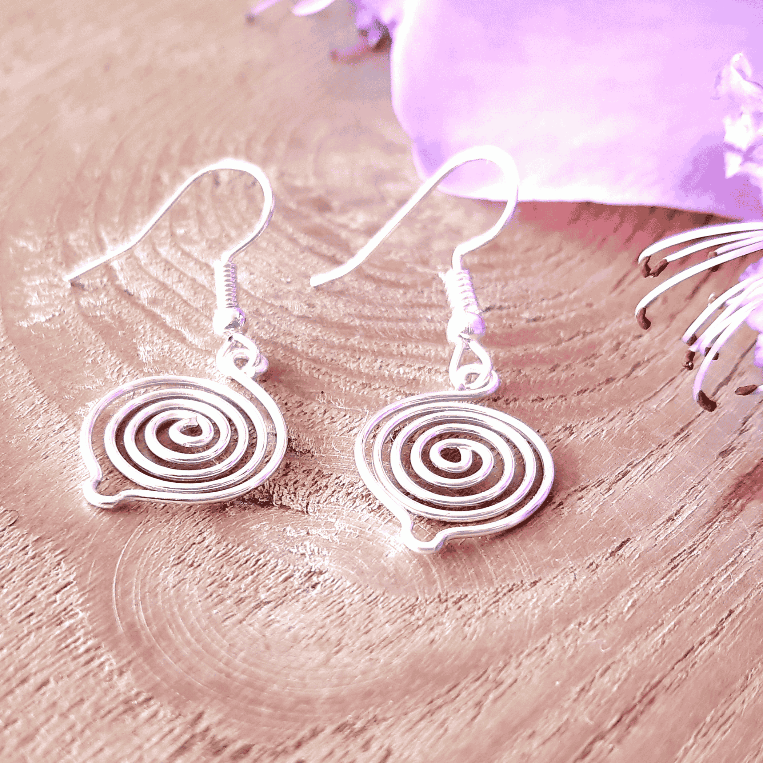 Silver spiral earrings on a pink wooden surface with a purple fabric background
