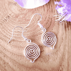 Silver spiral earrings on a wooden surface with purple flowers.