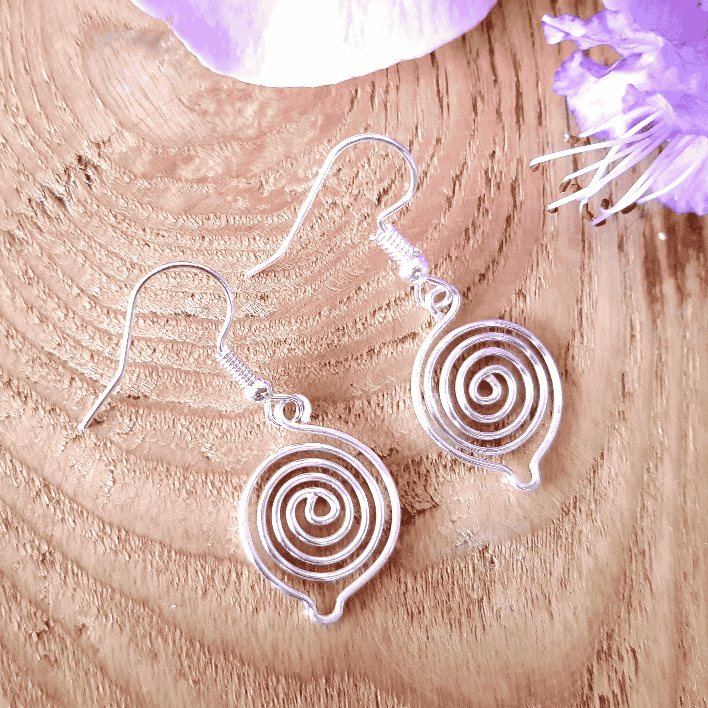 Silver spiral earrings on a wooden surface with purple flowers.