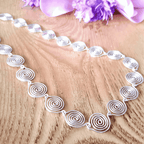Silver spiral necklace on a wooden surface with purple flowers in the background
