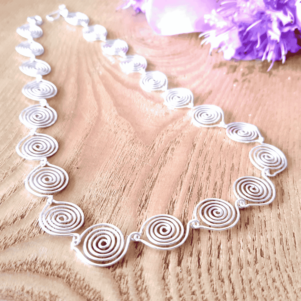 Tear drop shaped spiral form a chain to make this silver spiral necklace on a wooden brackground with purple flowers