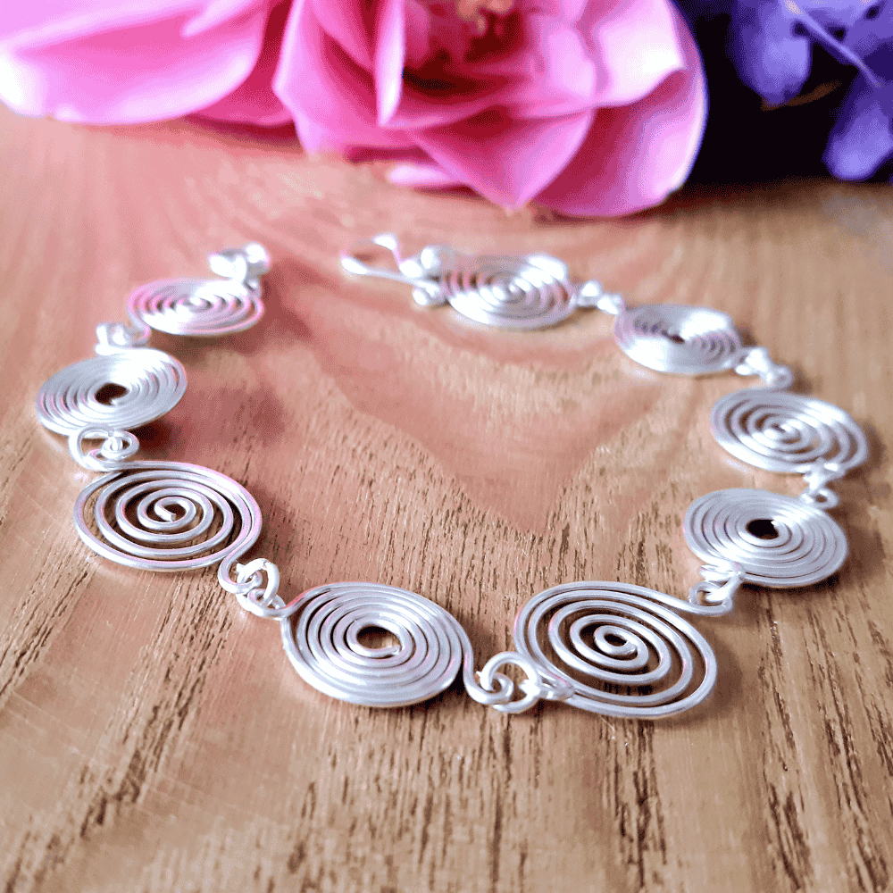 Open silver spiral bracelet on light wood background, handmade UK jewellery