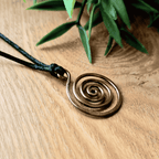 Bronzed copper spiral pendant on a black cord with green leaves in the background