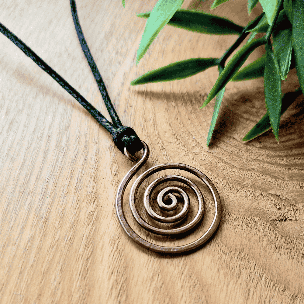 Bronzed copper spiral pendant on a black cord with green leaves in the background