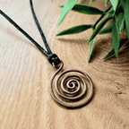 Bronzed copper spiral pendant on a black cord with green leaves in the background