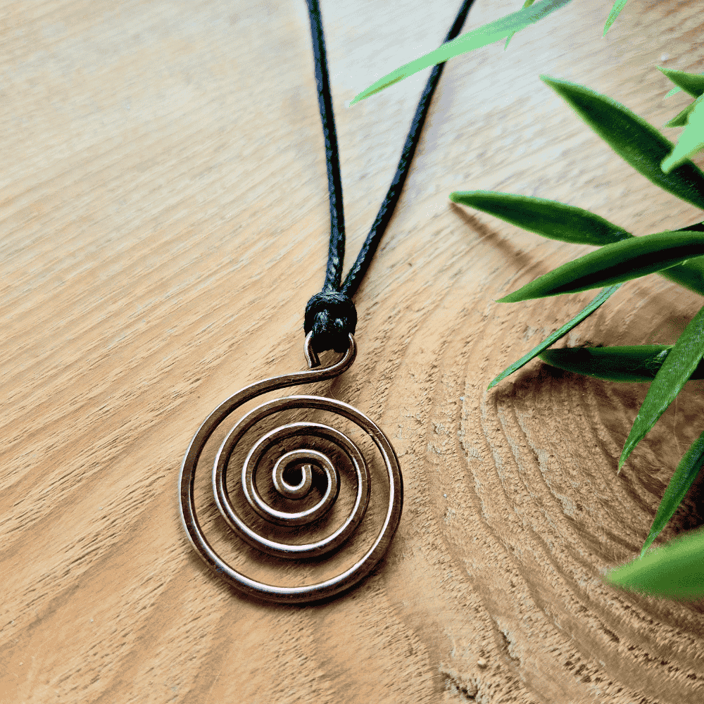 Necklace with a spiral pendant on a wooden surface with green leaves.