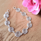 Open silver spiral bracelet, close-up detail on light wood background, handmade UK