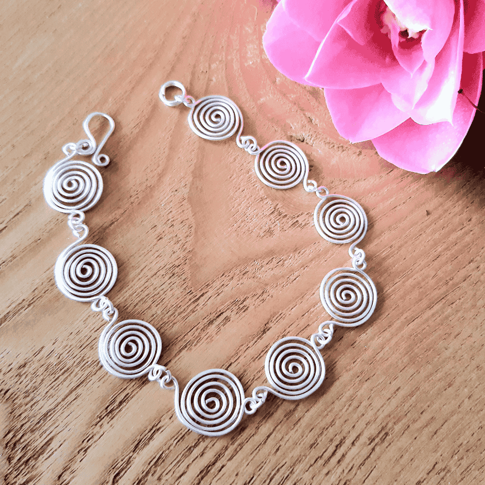 Open silver spiral bracelet, close-up detail on light wood background, handmade UK