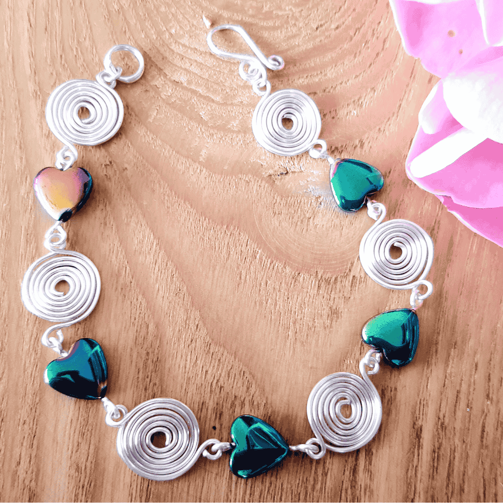 Silver bracelet with green heart-shaped beads on a wooden surface