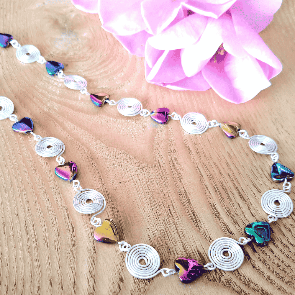 Necklace with heart-shaped beads and silver spirals on a wooden surface with pink flowers