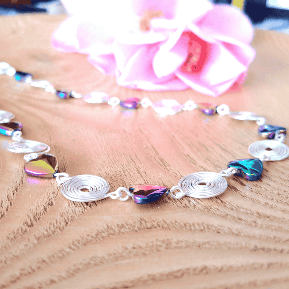 Necklace with colourful heart-shaped hematite beads and silver spirals on a wooden surface