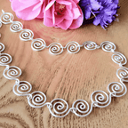 Silver spiral necklace on a wooden surface with pink and purple flowers.