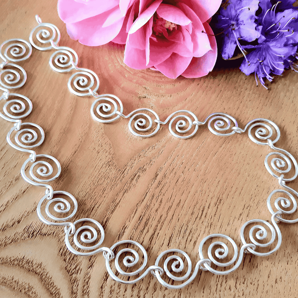 Decorative white metal necklace on a wooden surface with pink and purple flowers.
