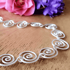 Silver wire spiral necklace on a wooden surface with pink and purple flowers in the background