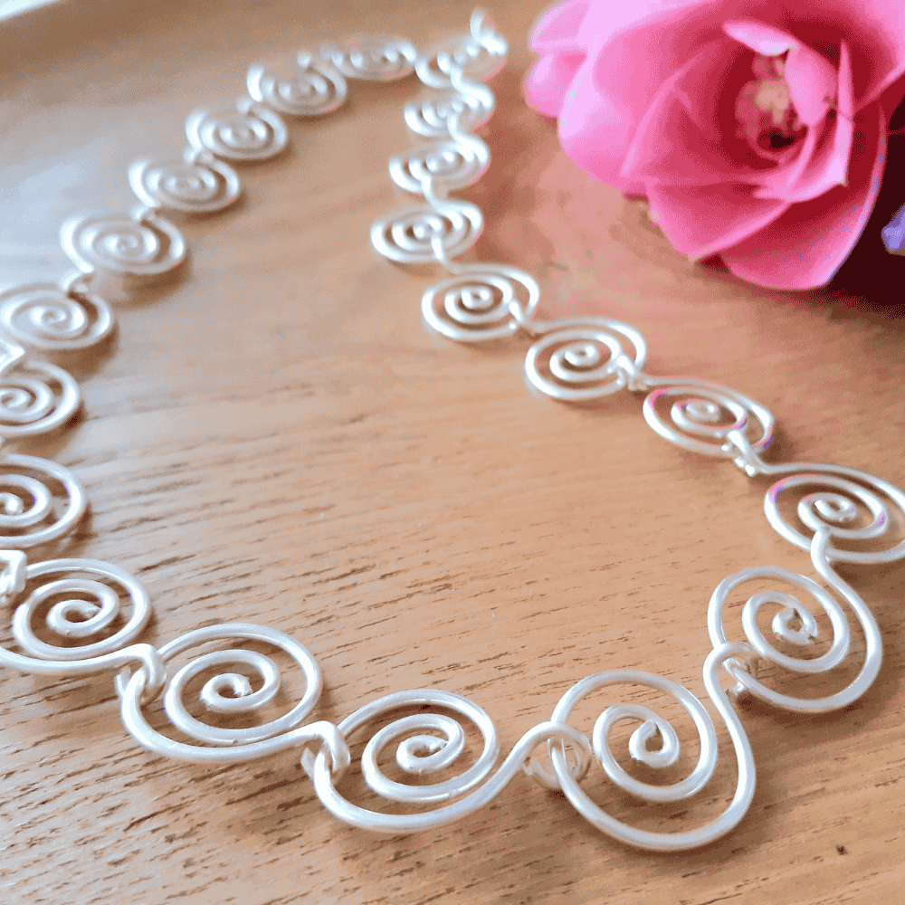 Silver wire necklace on a wooden surface with a pink rose.